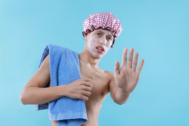 Photo of Man with shower cap and towel making stop gesture on light blue background