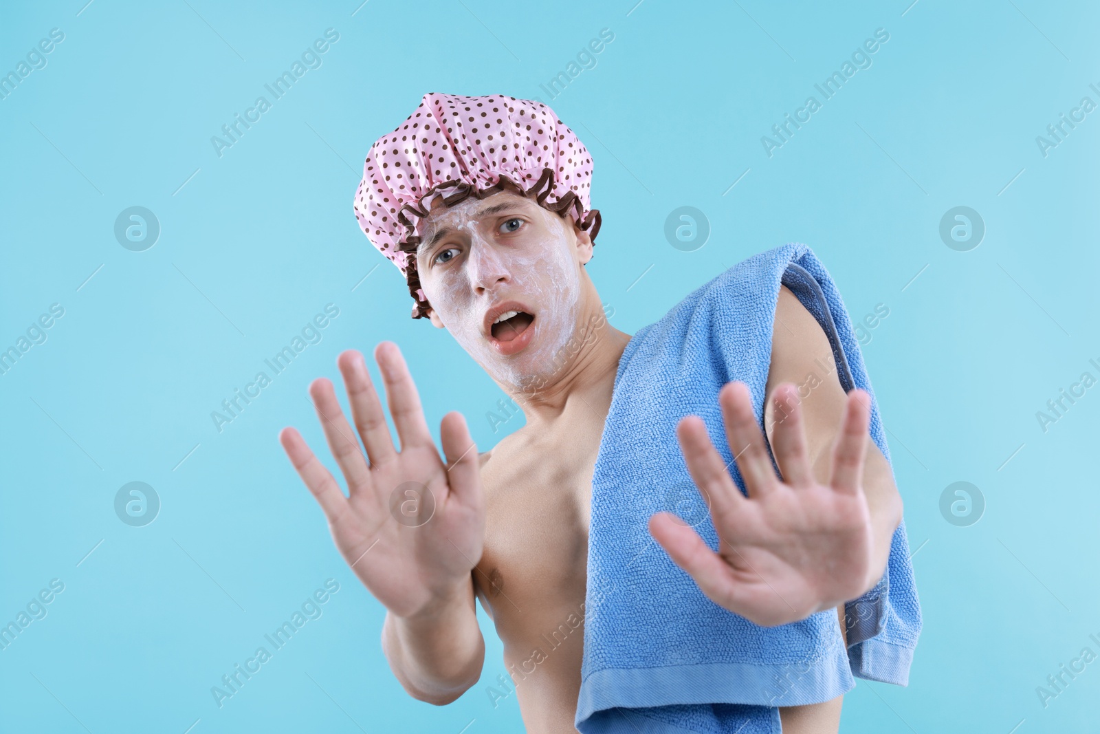 Photo of Man with shower cap and towel making stop gesture on light blue background