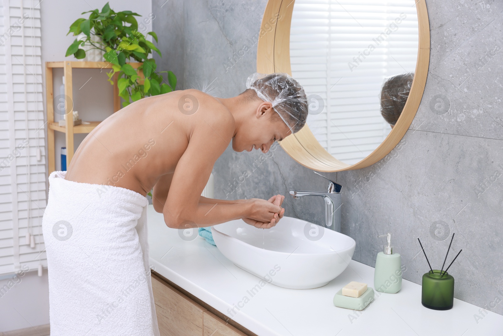 Photo of Man wearing shower cap washing his face in bathroom