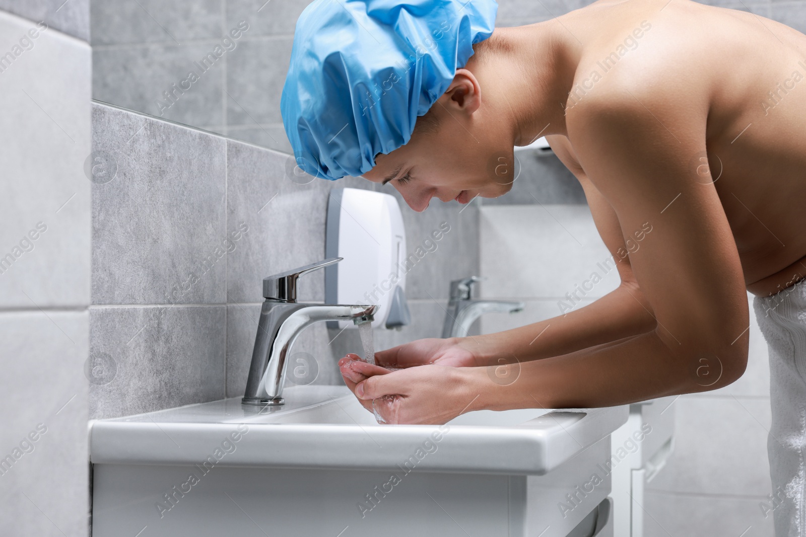 Photo of Man wearing shower cap washing his face in bathroom