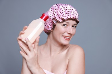 Photo of Woman with pink shower cap and shampoo on grey background