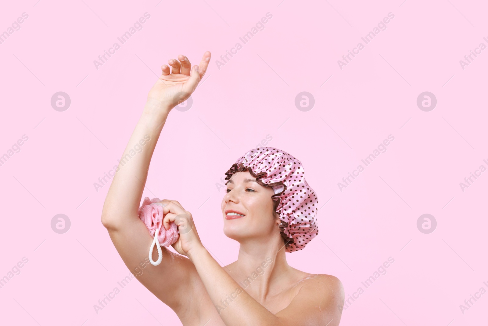 Photo of Woman with shower cap and mesh sponge on pink background