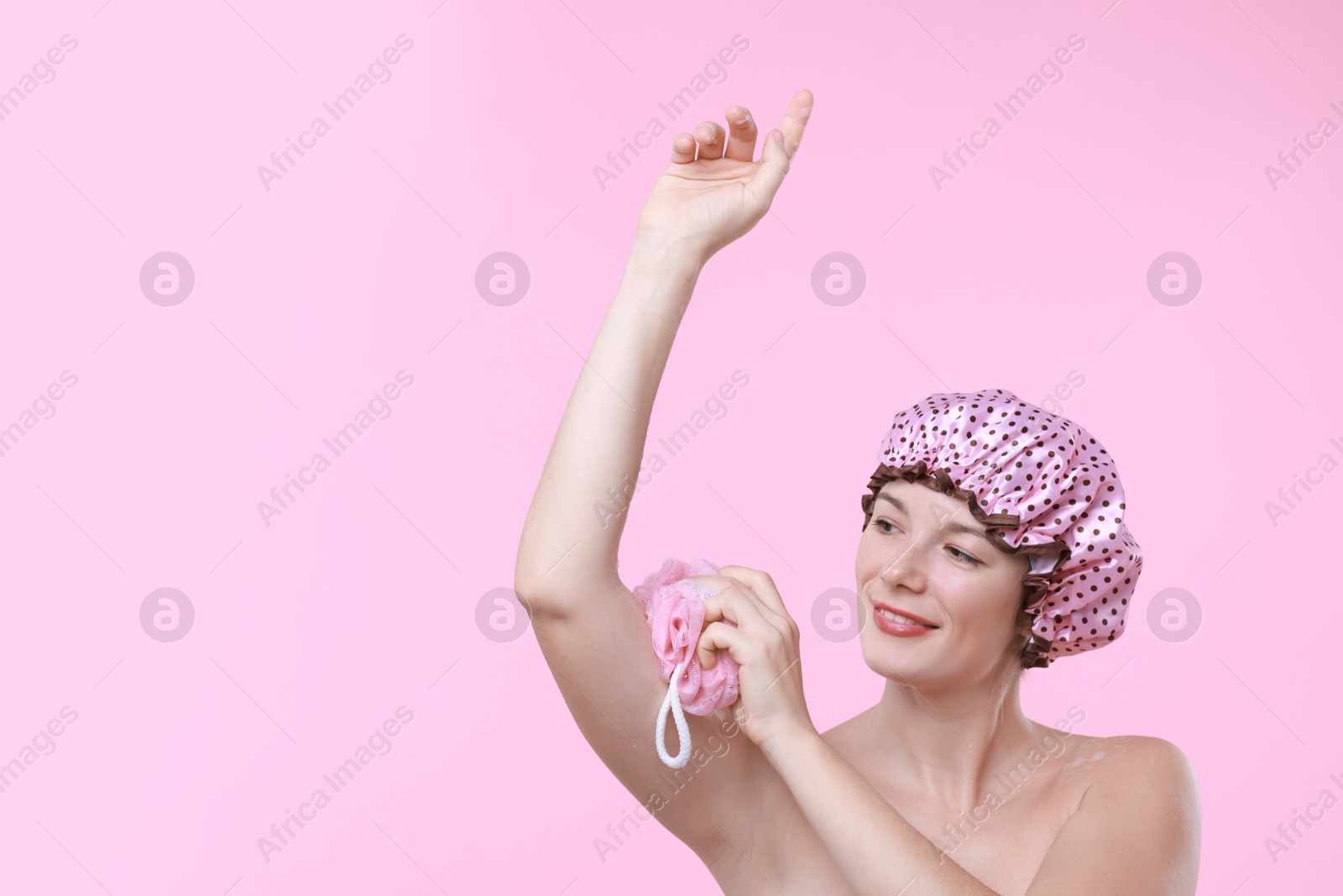 Photo of Woman with shower cap and mesh sponge on pink background, space for text