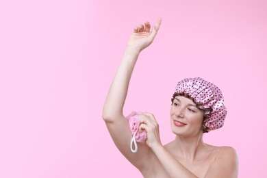 Photo of Woman with shower cap and mesh sponge on pink background, space for text