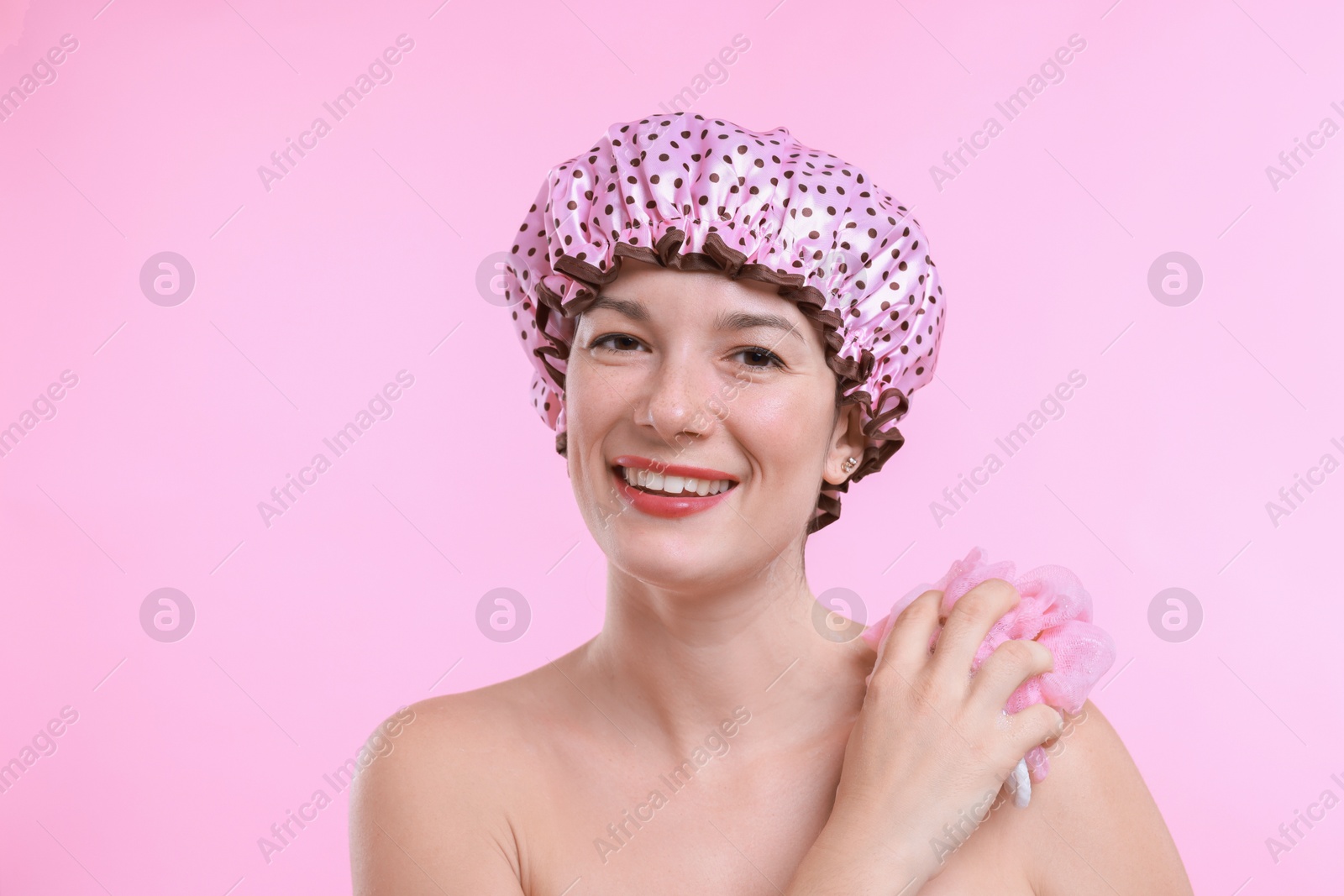 Photo of Woman with shower cap and mesh sponge on pink background