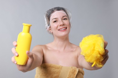 Photo of Woman with shower cap, shampoo and mesh sponge on grey background