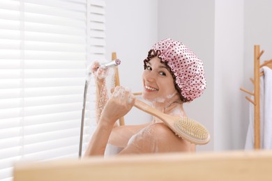 Photo of Woman with cap and brush taking shower in bathroom