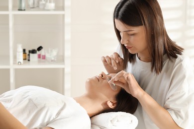 Photo of Esthetician brushing woman's lash extensions during procedure in beauty salon