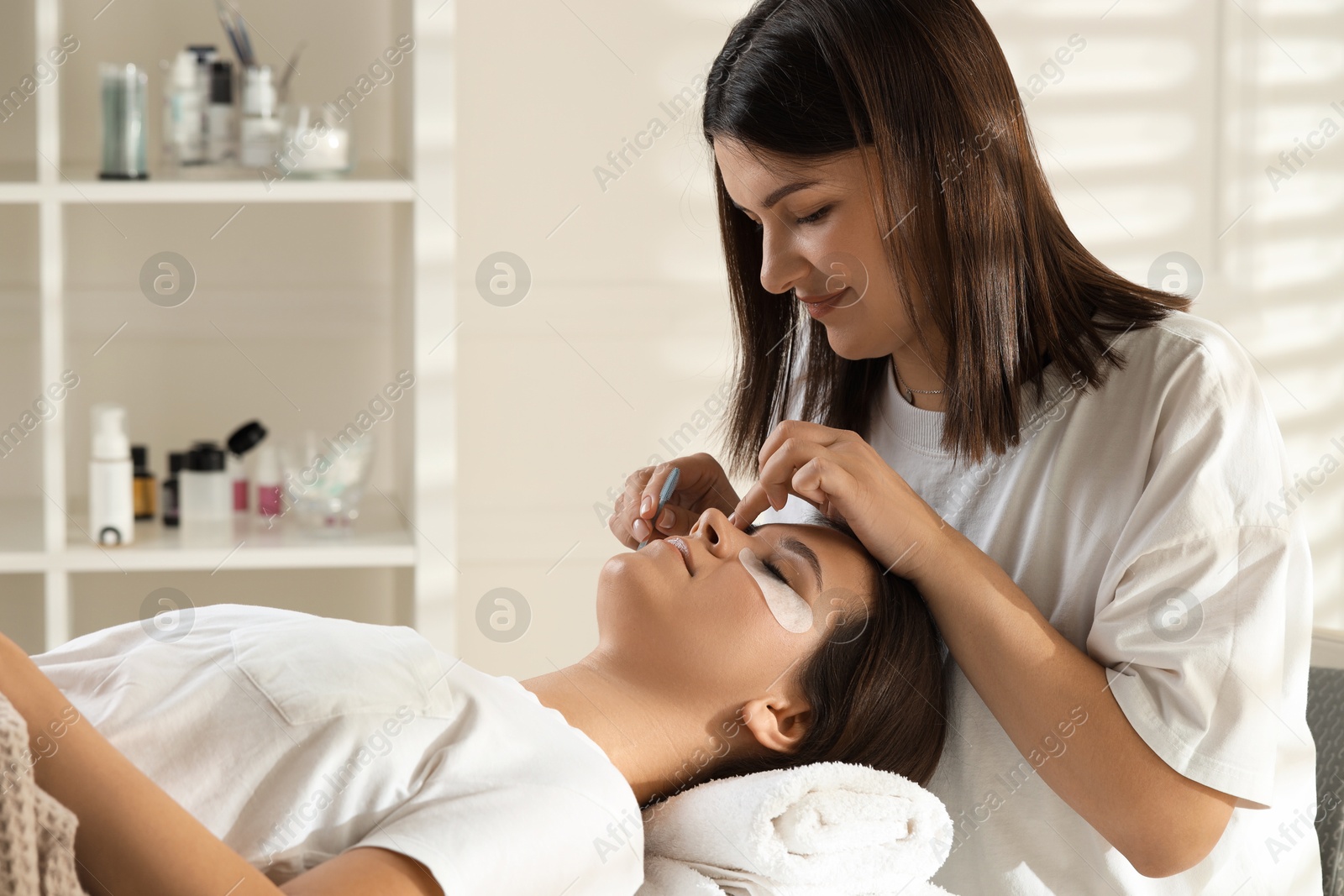 Photo of Esthetician brushing woman's lash extensions during procedure in beauty salon