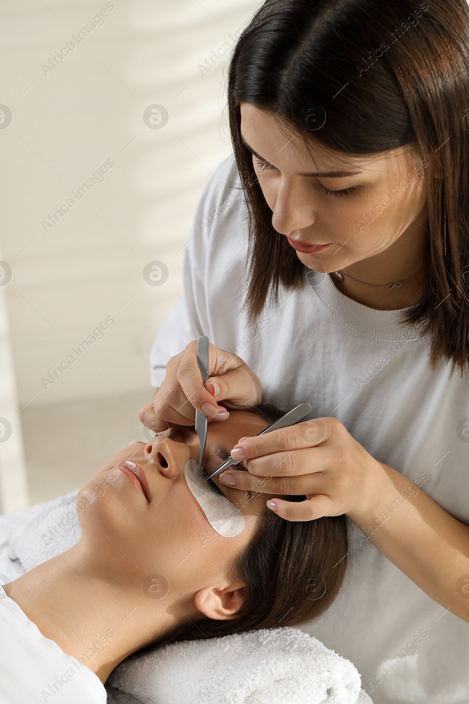 Photo of Esthetician applying lash extensions on natural ones in beauty salon, closeup