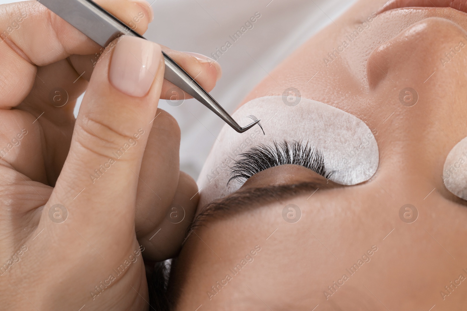 Photo of Woman undergoing lash extensions procedure in beauty salon, closeup