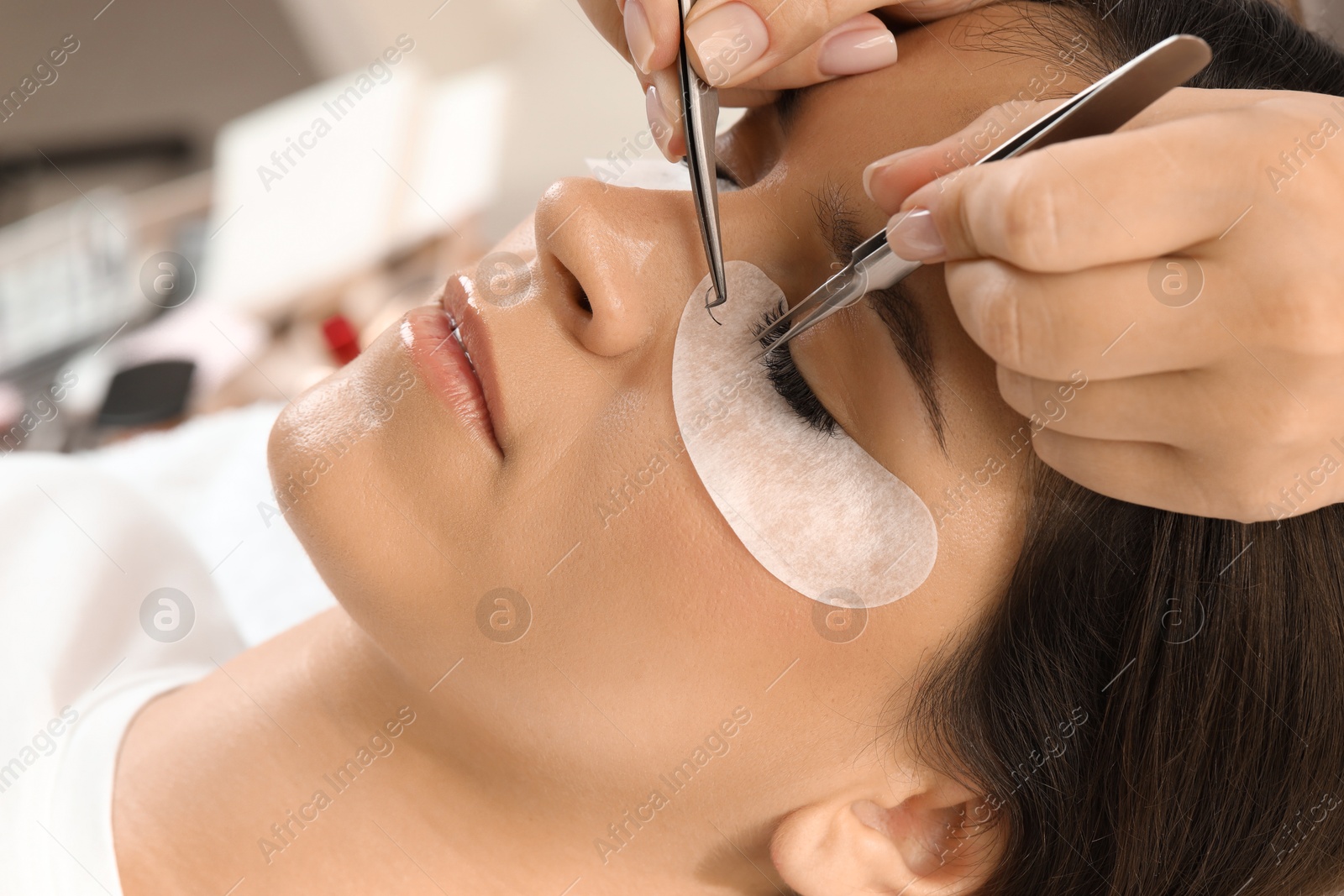 Photo of Woman undergoing lash extensions procedure in beauty salon, closeup