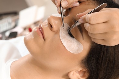 Woman undergoing lash extensions procedure in beauty salon, closeup