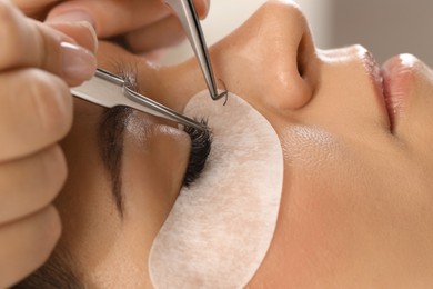 Photo of Woman undergoing lash extensions procedure in beauty salon, closeup