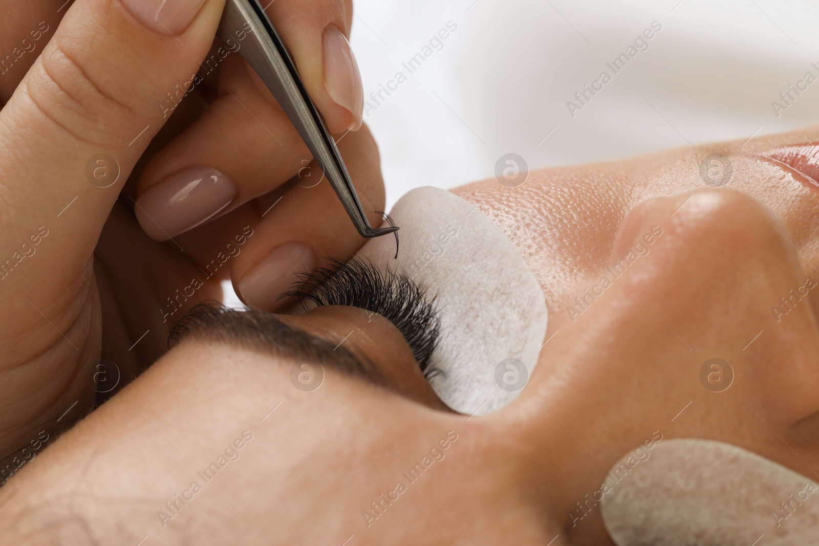 Photo of Woman undergoing lash extensions procedure in beauty salon, closeup