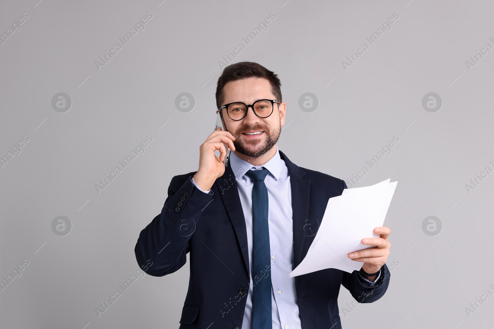 Photo of Banker with documents talking on smartphone against grey background