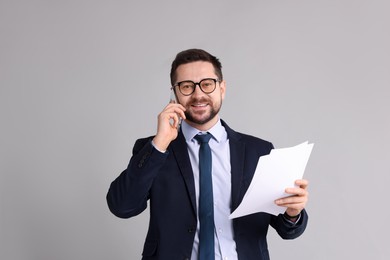 Banker with documents talking on smartphone against grey background