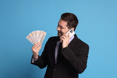 Photo of Banker with dollar banknotes talking on smartphone against light blue background