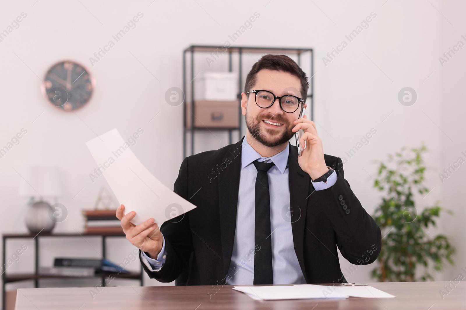 Photo of Banker with document talking on smartphone at wooden table in office