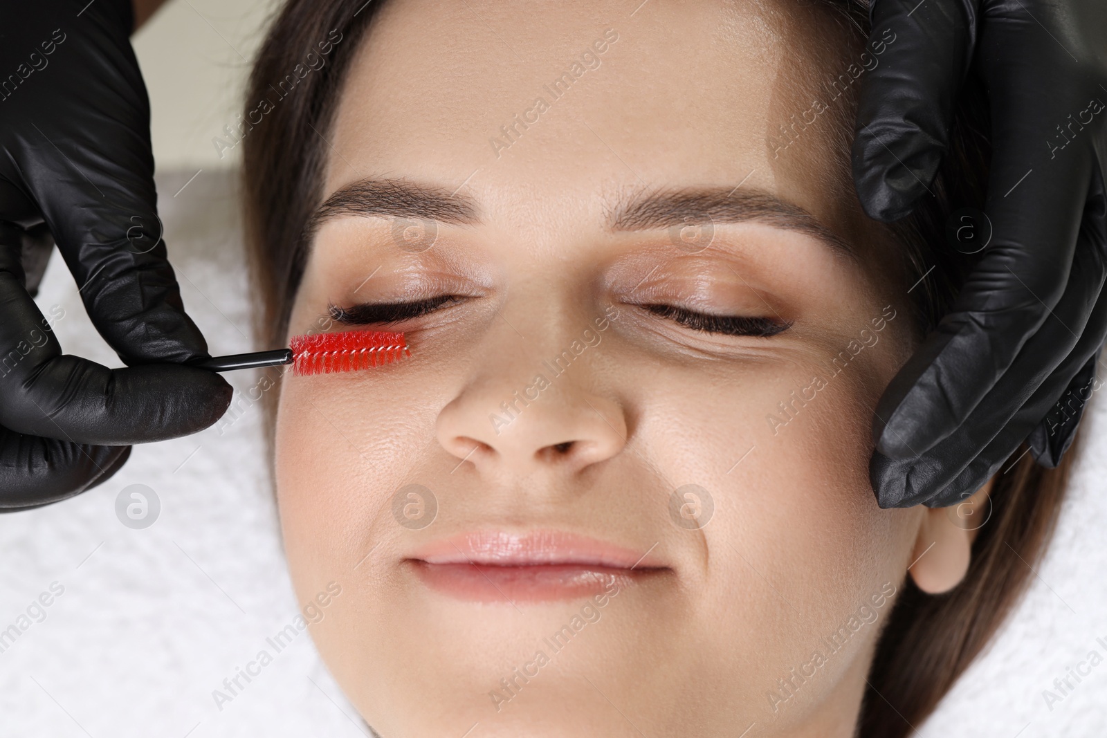 Photo of Eyelash extension procedure. Esthetician combing woman's lashes with brush in beauty salon, top view