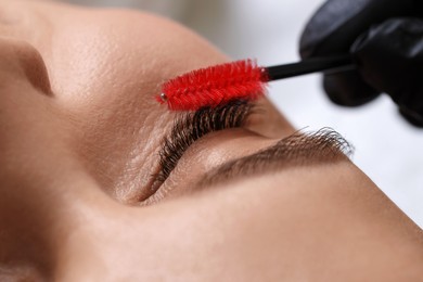 Photo of Eyelash extension procedure. Esthetician combing woman's lashes with brush in beauty salon, closeup