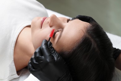 Eyelash extension procedure. Esthetician combing woman's lashes with brush in beauty salon, closeup