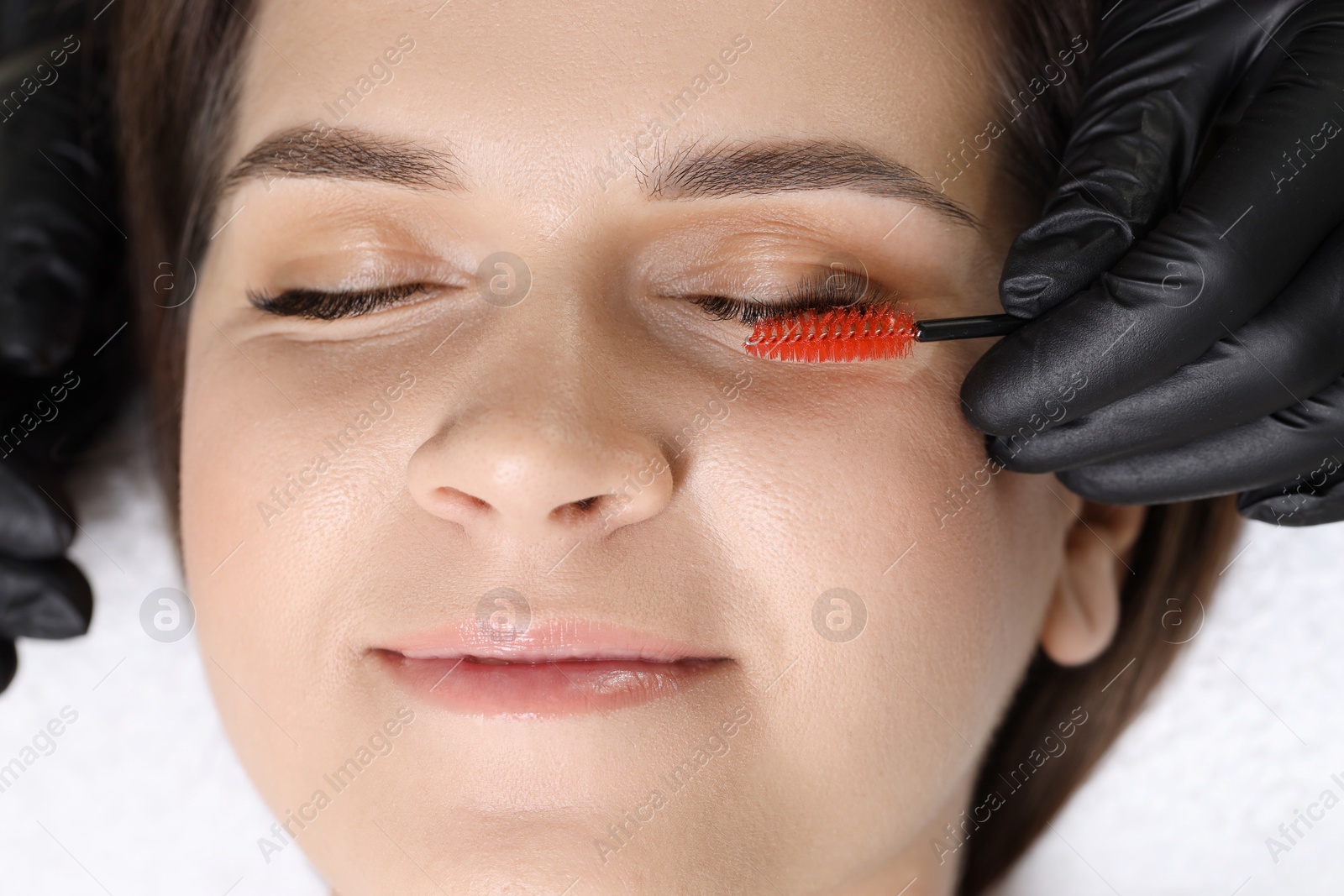 Photo of Eyelash extension procedure. Esthetician combing woman's lashes with brush in beauty salon, top view