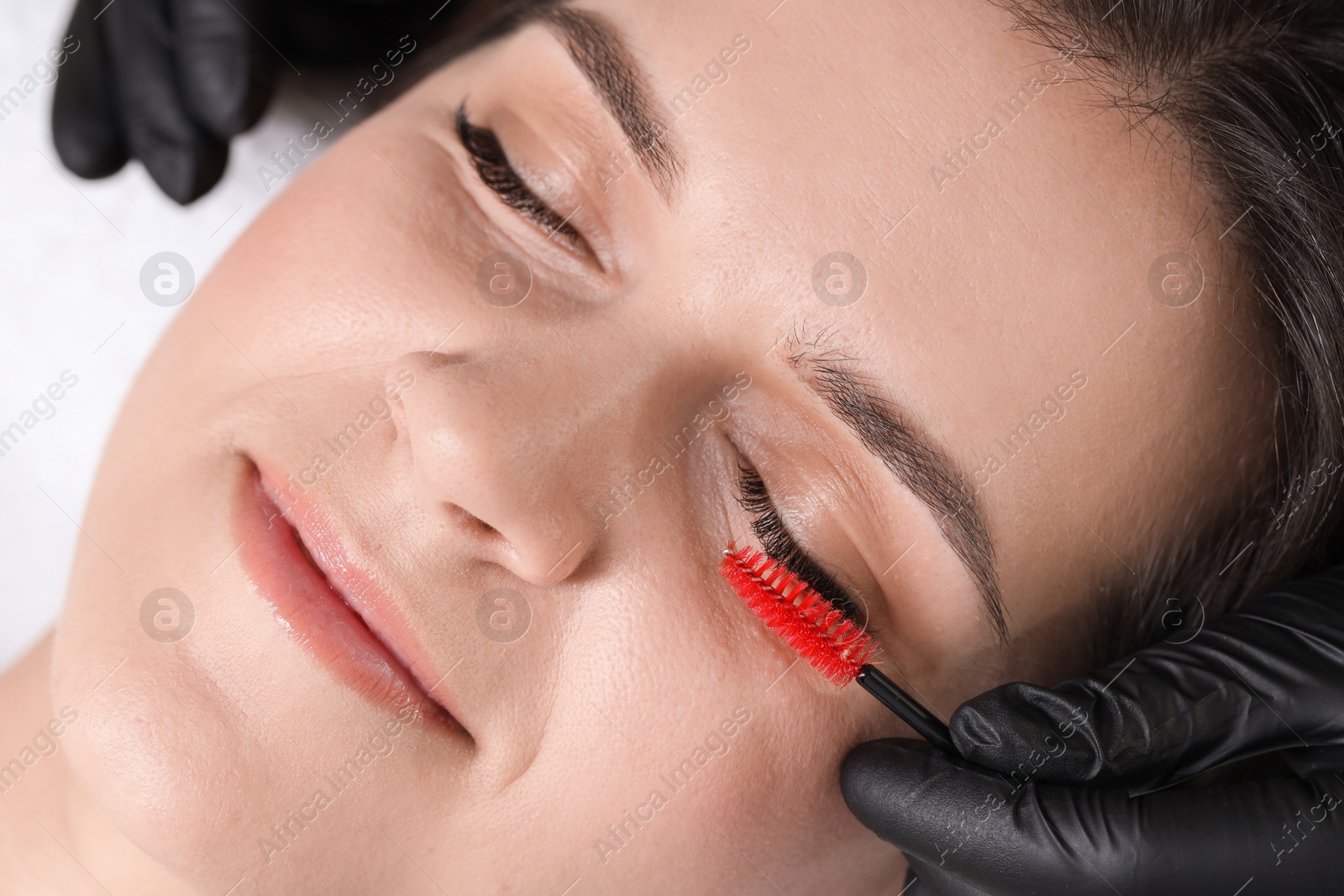 Photo of Eyelash extension procedure. Esthetician combing woman's lashes with brush in beauty salon, closeup