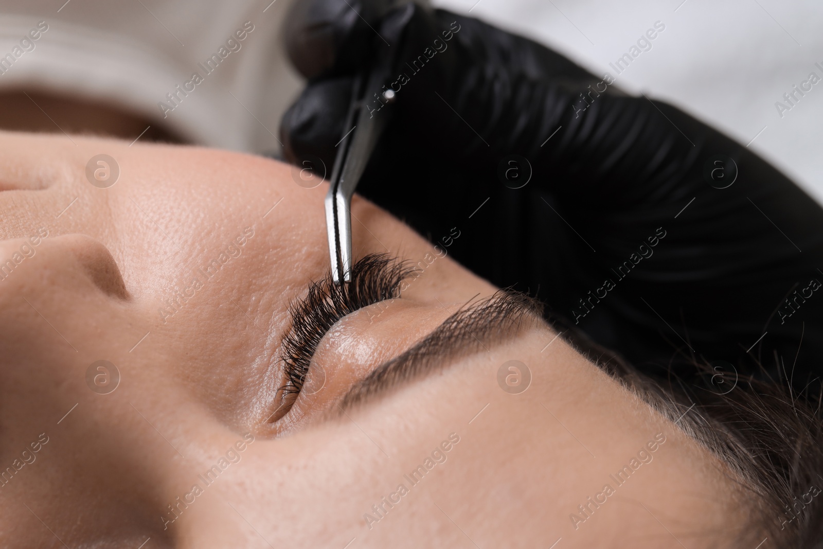 Photo of Woman undergoing lash extensions procedure in beauty salon, closeup