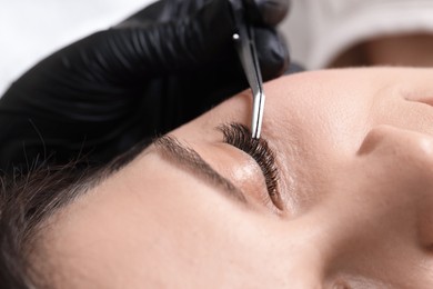 Photo of Woman undergoing lash extensions procedure in beauty salon, closeup