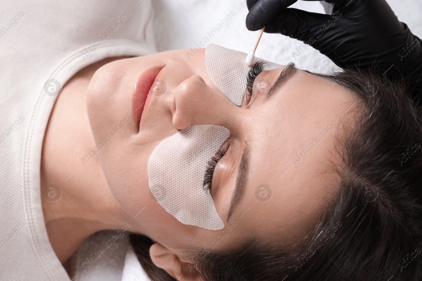 Photo of Woman undergoing lash extensions procedure in beauty salon, closeup