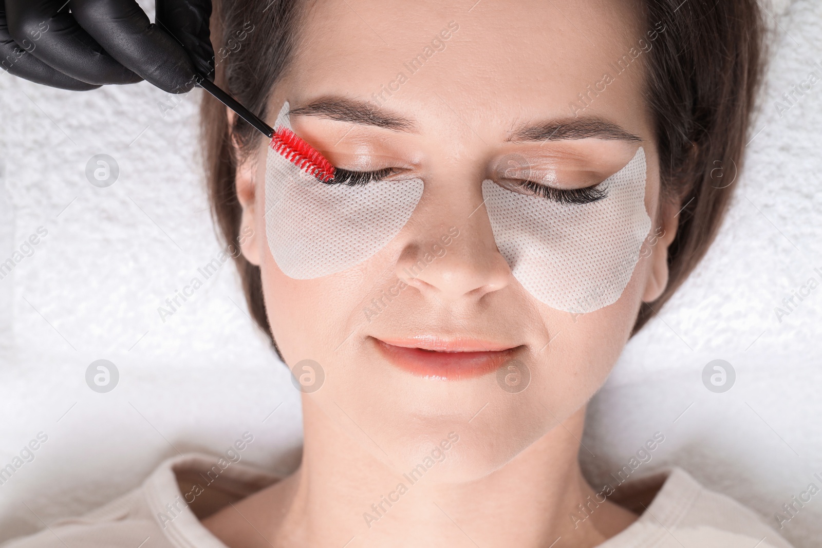 Photo of Eyelash extension procedure. Esthetician combing woman's lashes with brush in beauty salon, top view