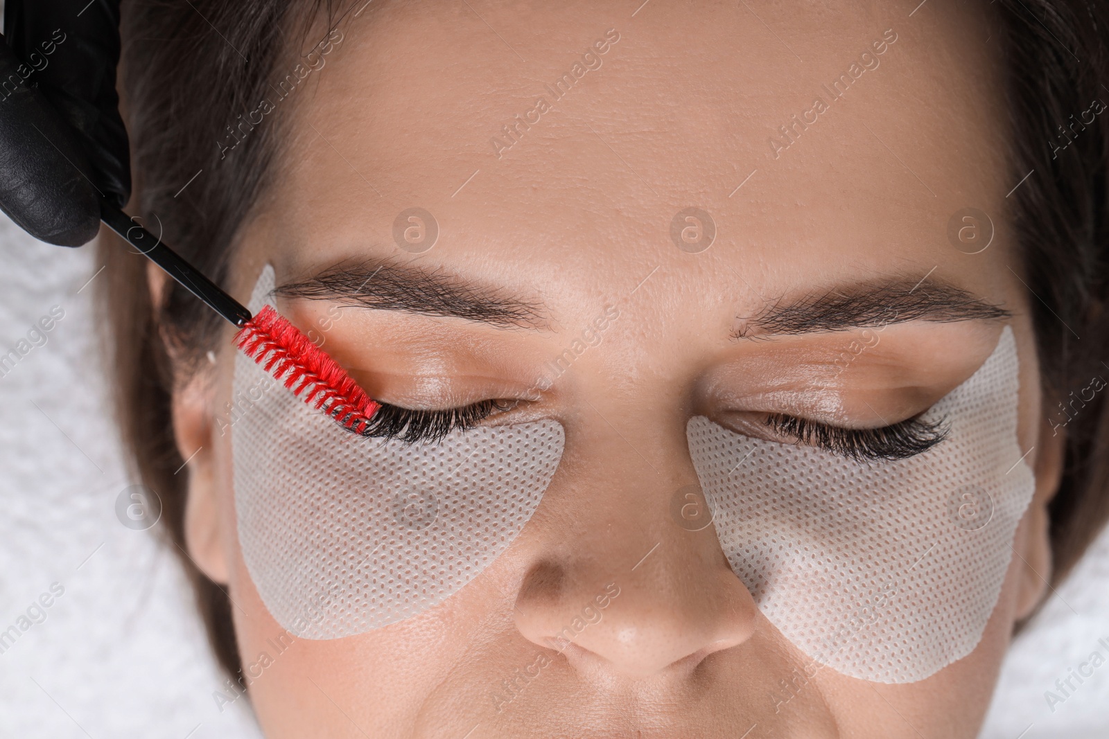 Photo of Eyelash extension procedure. Esthetician combing woman's lashes with brush in beauty salon, top view