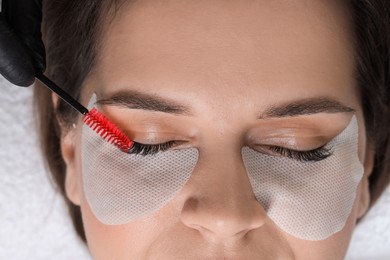 Photo of Eyelash extension procedure. Esthetician combing woman's lashes with brush in beauty salon, top view