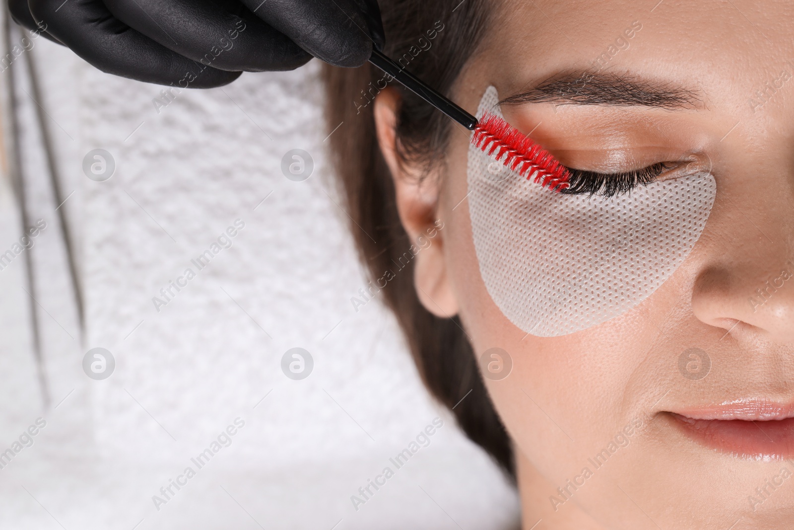 Photo of Eyelash extension procedure. Esthetician combing woman's lashes with brush in beauty salon, top view. Space for text