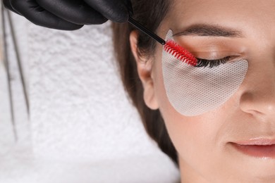 Photo of Eyelash extension procedure. Esthetician combing woman's lashes with brush in beauty salon, top view. Space for text