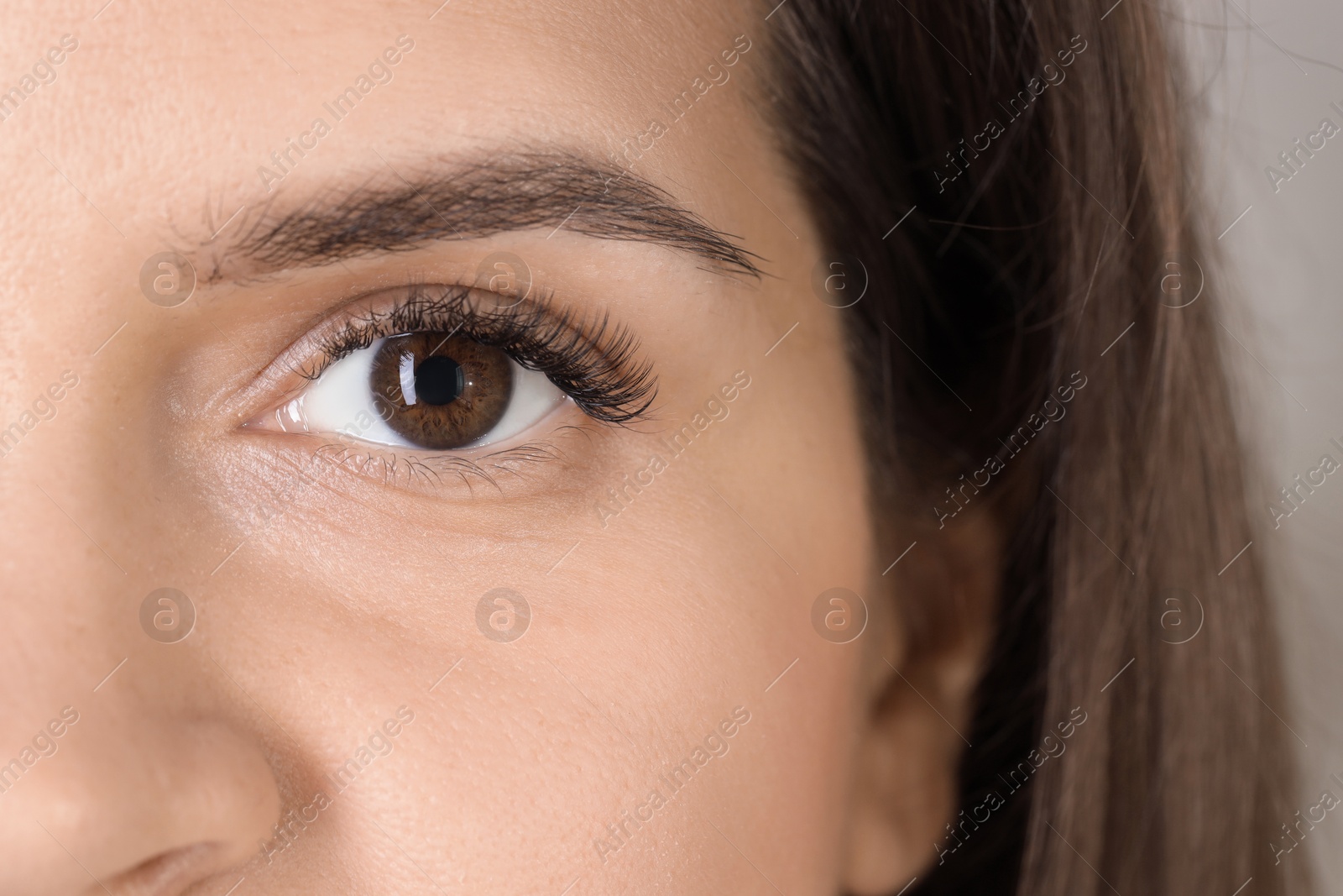 Photo of Woman with beautiful long eyelashes on light background, closeup. Eyelash extension procedure