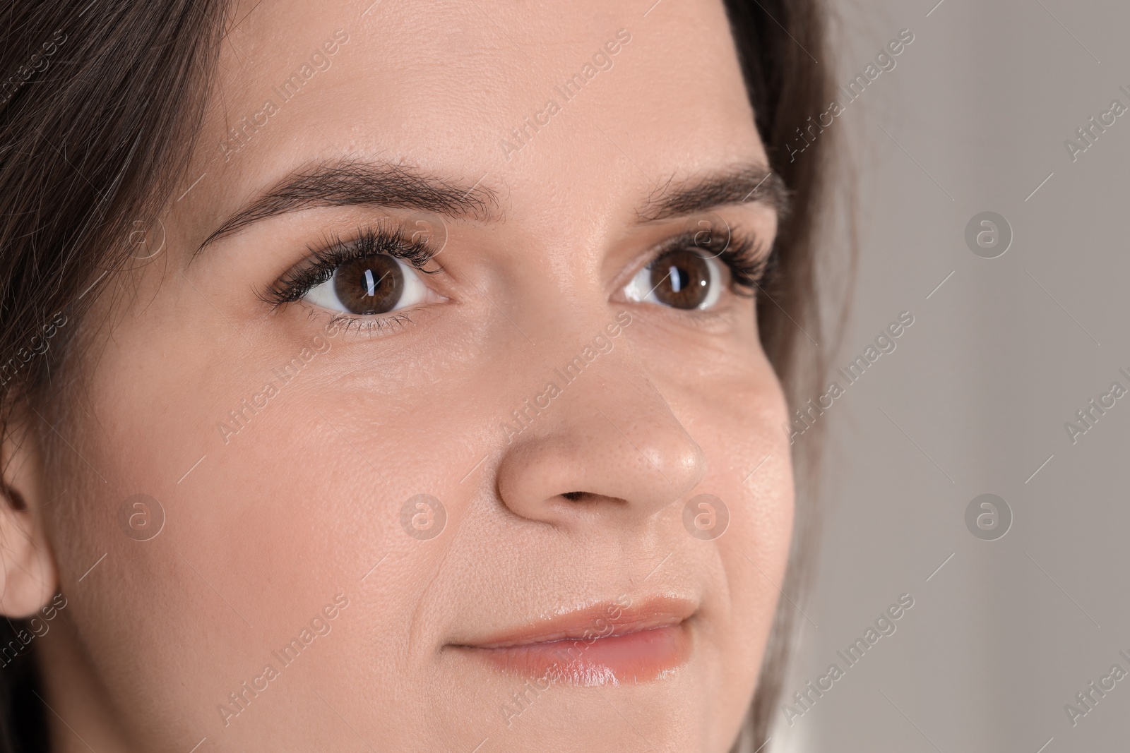 Photo of Woman with beautiful long eyelashes on grey background, closeup. Eyelash extension procedure