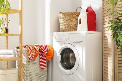 Photo of Wicker basket full of laundry, washing machine and detergents in bathroom