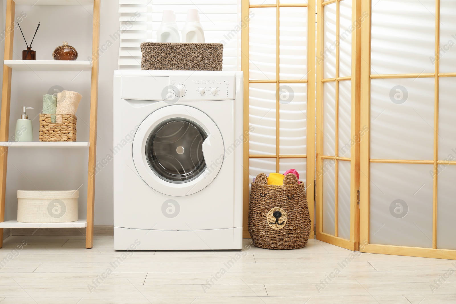 Photo of Wicker basket full of laundry, washing machine and detergents in bathroom