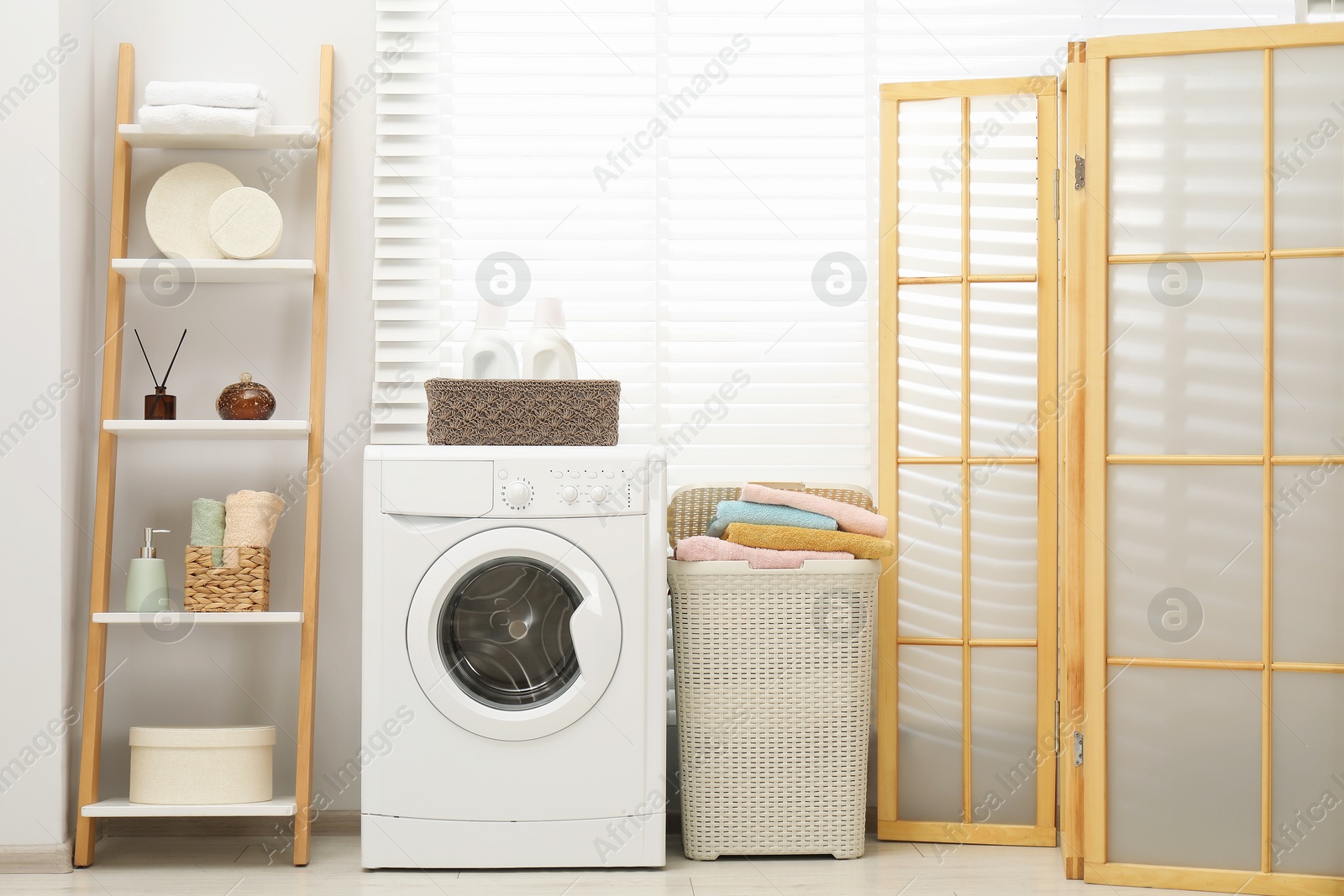 Photo of Wicker basket full of laundry, washing machine and detergents in bathroom