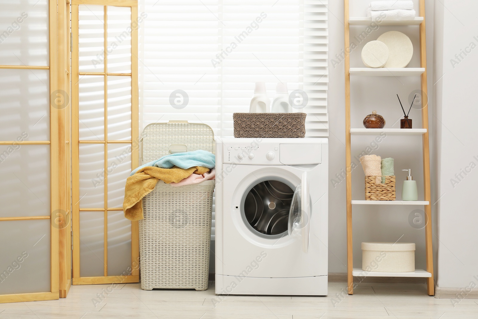 Photo of Wicker basket full of laundry, washing machine and detergents in bathroom