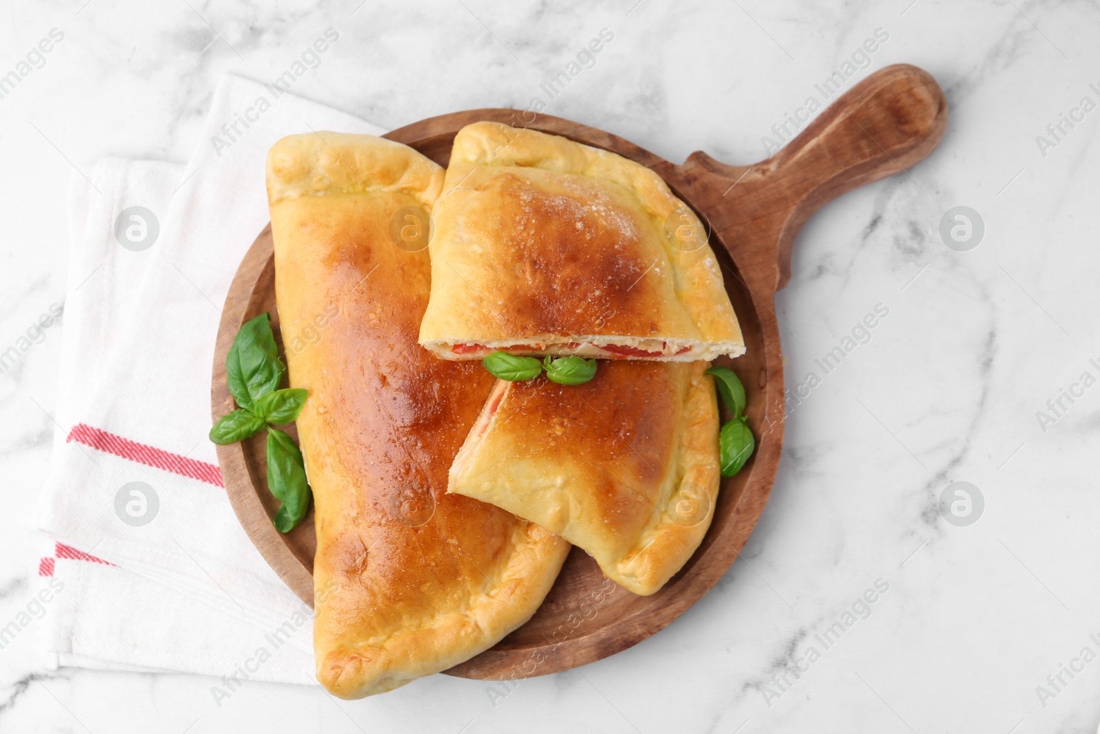 Photo of Tasty vegetarian calzones with tomato, cheese and basil on white marble table, top view