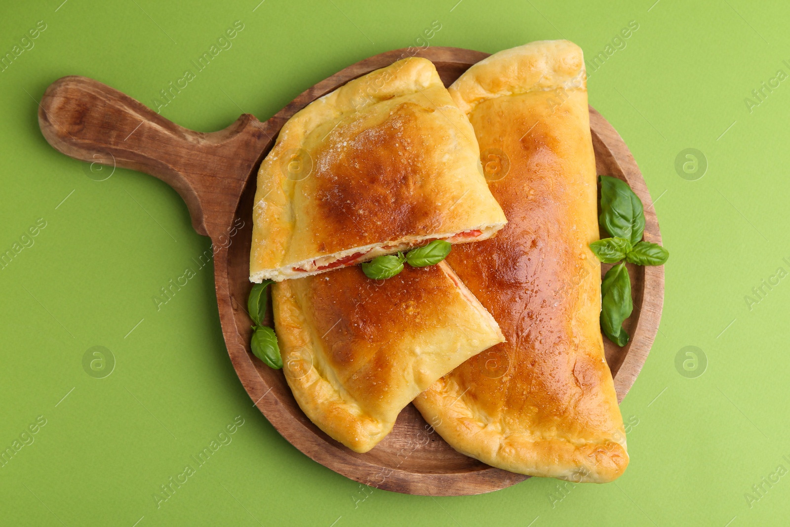 Photo of Tasty vegetarian calzones with tomato, cheese and basil on green background, top view