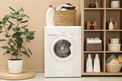 Photo of Wicker basket full of laundry, washing machine and detergent in bathroom