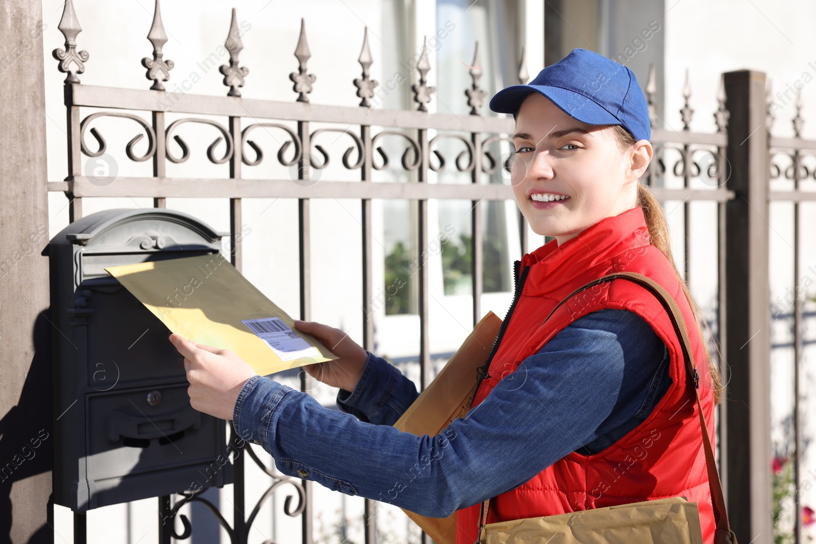 Photo of Postwoman putting envelope into mail box outdoors