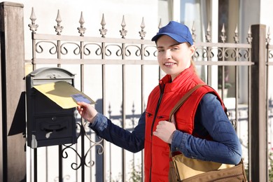 Photo of Postwoman putting envelope into mail box outdoors