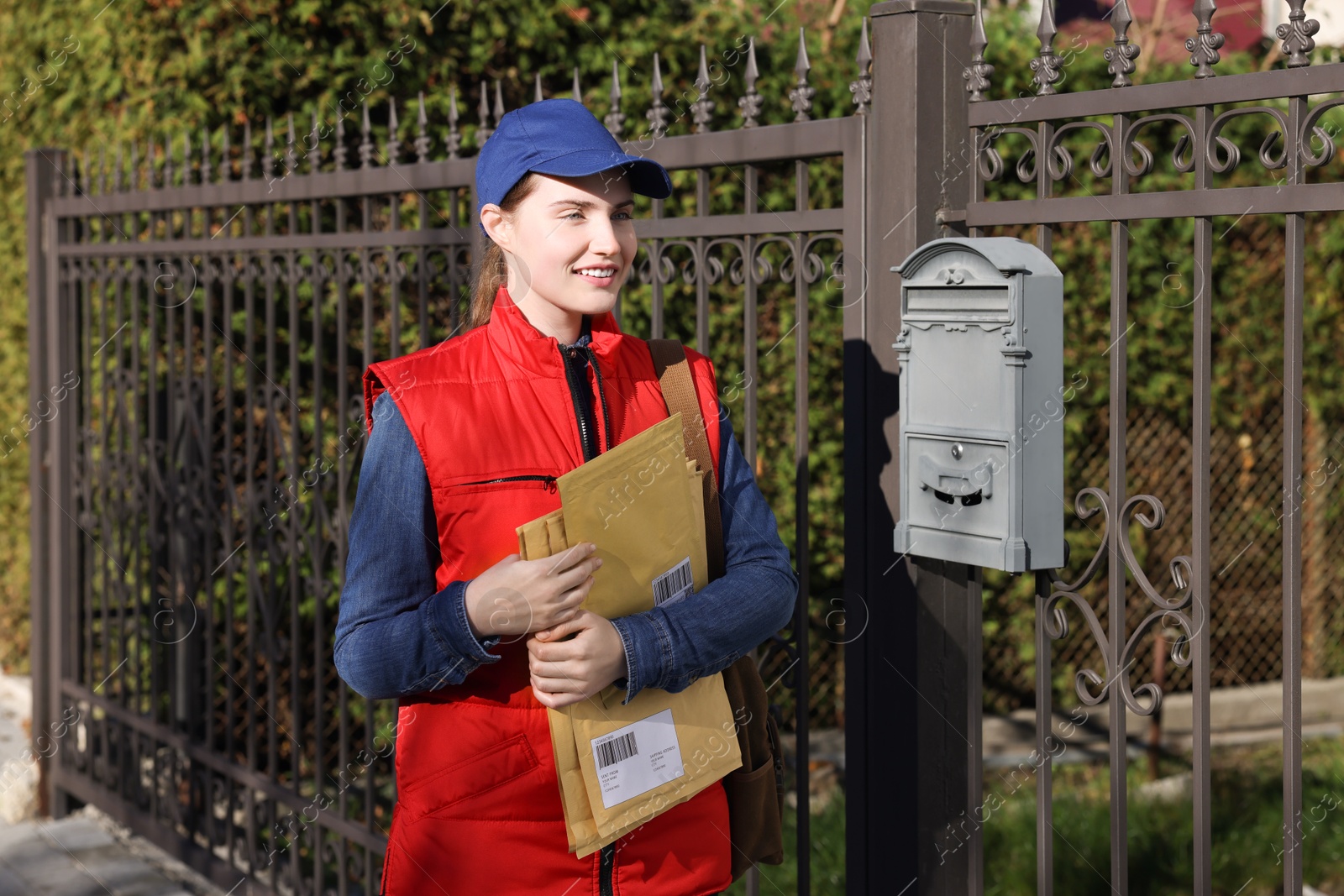 Photo of Mailwoman in uniform with envelopes outdoors. Postal service