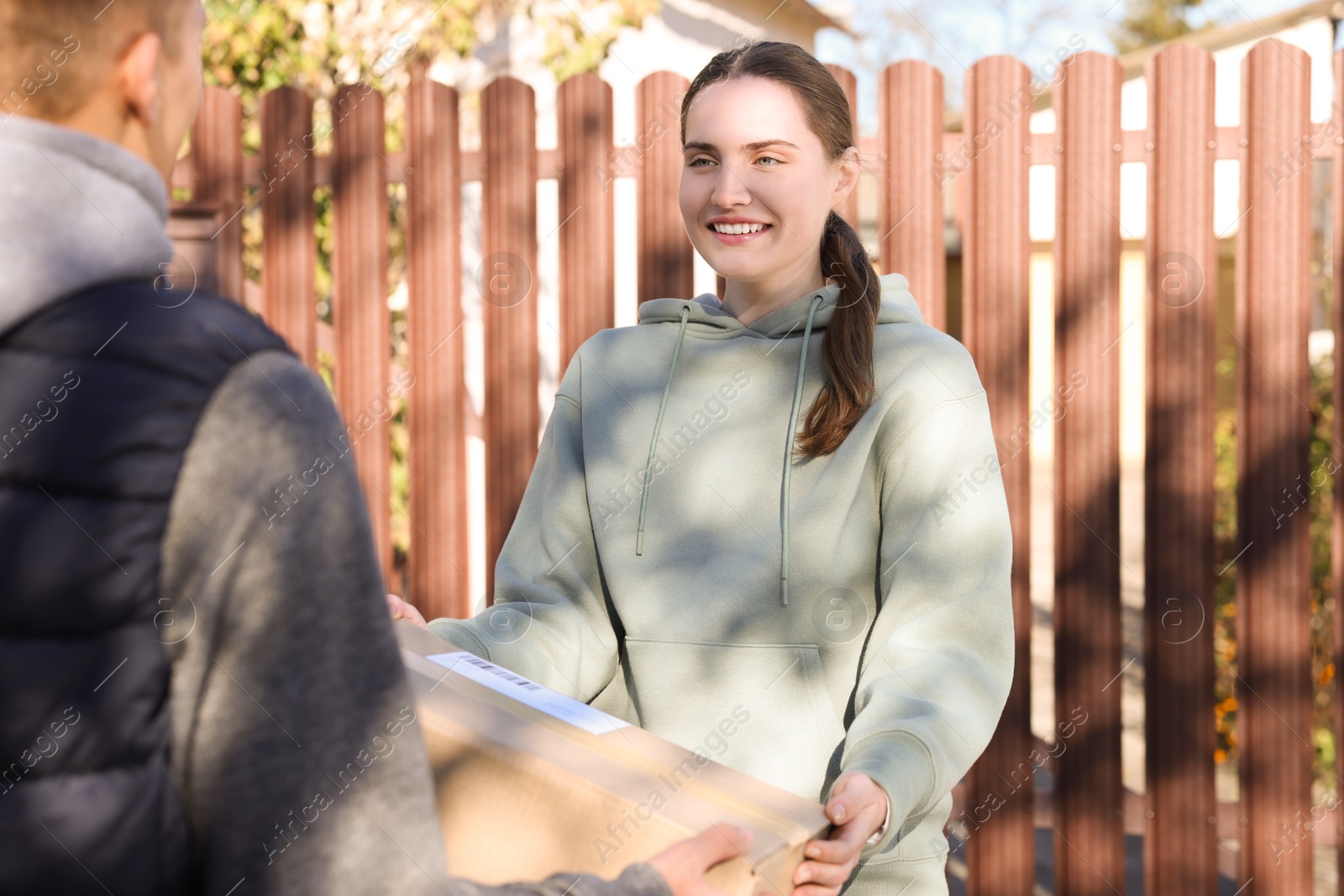 Photo of Postman giving parcel box to woman outdoors