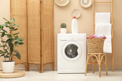 Photo of Wicker basket full of laundry, washing machine and detergent in bathroom